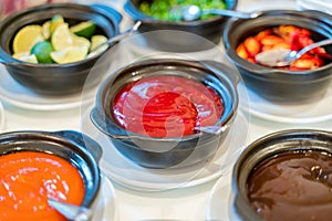 Various bowls of assorted sauces, dips on a asian cuisine buffet