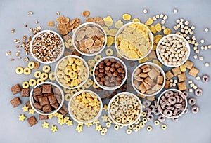 Various breakfast cereals on light grey background, assorted corn flakes in bowls