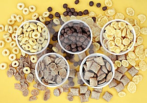 Various breakfast cereals on yellow bright background, assorted corn flakes in bowls