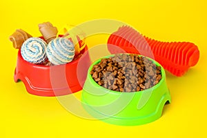 Various bright pet toys and bowl of food on yellow background