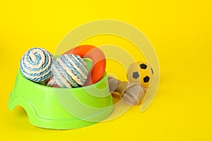 Various bright pet toys and bowl on yellow background, space for text