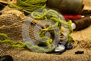 Various buttons and multicolored threads on coarse-textured burlap. Close up