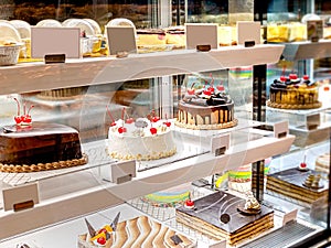 Various Cake with Icing in Refrigerated Bakery Case Cabinet. Chocolate and Cherry Tart Toping on Fridge Display