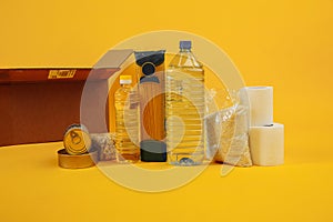 Various canned food, pasta and cereals in a cardboard box on a yellow background. Food donations or food delivery