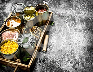 Various canned products in tin cans on a wooden tray.