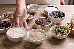 Various cereal grain in a bowl with hand on wooden table