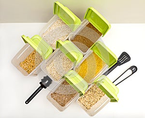 Various cereals - wheat, peas, buckwheat, millet, oatmeal, barley out of focus in open plastic containers with green lids for bulk