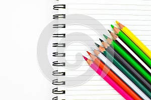 Various colored pencil crayons placed in a waved form row before a diary