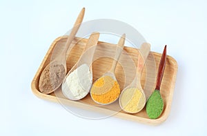 Various colorful powder in different wooden spoons on wood tray isolated on white background