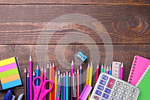 Various colorful school and office supplies on a brown wooden table.