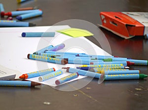 Various colors wax crayons with paper at desk