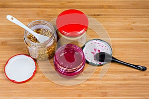 Various condiments in small glass jars on a wooden surface