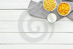 Various corn cereals in bowls and milk on white wooden background top view copyspace