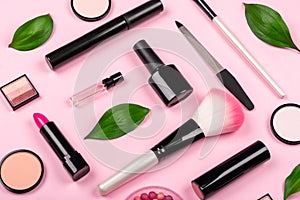Various cosmetic accessories for makeup and manicure on pink background with fresh green leaves. Skin care products.