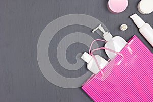 Various cosmetic products with pink paper bag on grey wood desk - top view. Buying cosmetics. Beauty shopping background