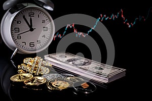 Various crypto coins lie next to a stack of 100-dollar bills, a white alarm clock and a diamond-studded dollar chain pendant