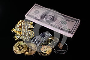 Various crypto coins lie next to a stack of 100-dollar bills, a white alarm clock and a diamond-studded dollar chain pendant