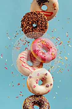 Various decorated doughnuts in motion falling on blue background