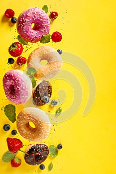 Various decorated doughnuts with sprinkles and berries in motion falling on yelloy background