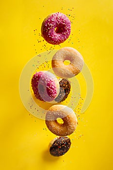 Various decorated doughnuts with sprinkles in motion falling on yelloy background