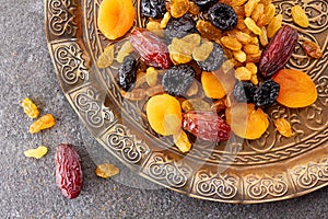 Various dried fruits on toreutic plate over stone background
