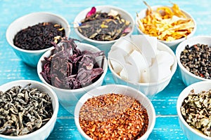 Various dried medicinal herbs and teas in several bowls on blue wooden background