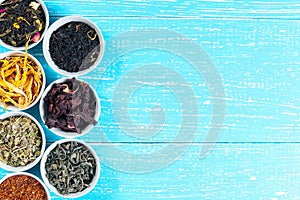 Various dried medicinal herbs and teas in several bowls on blue wooden background