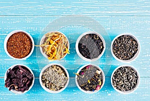 Various dried medicinal herbs and teas in several bowls on blue wooden background from above