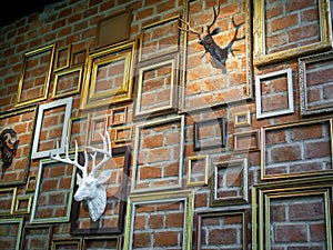 Various empty photo frames with plaster deer head hanging on brick wall