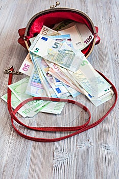 Various euro banknotes fall out from red handbag