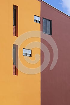 Various fixing glass windows on orange and brown modern building wall with blue sky in perspective side view