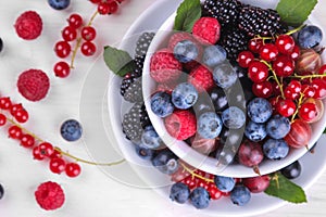 Various fresh berries close-up including blueberries, raspberries, blackberries and currants in a white cup on a white wooden back