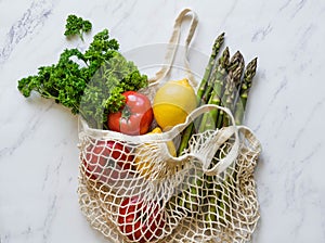 Various fresh food - vegetables and fruits in eco-friendly bag on white marble background. Vegetarian meal from the market in