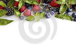 Various fresh summer berries on white background. Ripe raspberries, blackberries, blueberries, mint and basil leaves.