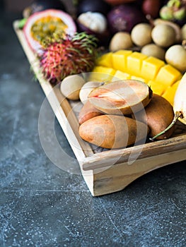 Various fresh Thai fruits - rambutan, mango, mangosteen, longan, sapodilla, passion fruit, salak, on a wooden tray and a gray