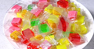 Various fruit candies in transparent packaging in a white plate on the table