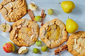 Various fruits tarts decorated with cinnamon sticks on the gray concrete background. Vegetarian healthy galette with fresh apples