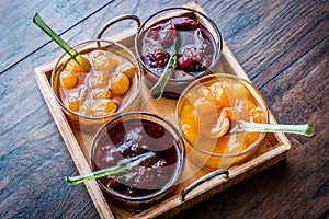 Various glass bowl of Fruit jams Apricot, cherry, strawberry, damson plum in wooden tray.