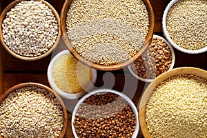 Various groats, cereals. Different types of groats in bowls on a wooden background, top view, close up.