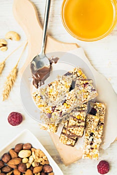 Various homemade granola bars with nuts, seeds, dark chocolate, honey and berries over a wooden board