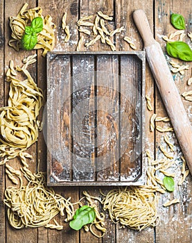 Various homemade uncooked Italian pasta and wooden tray in center