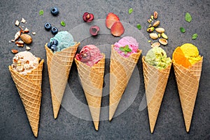 Various of ice cream flavor in cones blueberry ,strawberry ,pistachio ,almond ,orange and cherry setup on dark stone background .