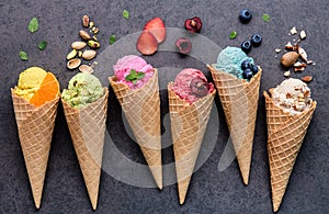 Various of ice cream flavor in cones blueberry ,strawberry ,pistachio ,almond ,orange and cherry setup on dark stone background .