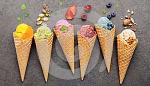 Various of ice cream flavor in cones blueberry ,strawberry ,pistachio ,almond ,orange and cherry setup on dark stone background .