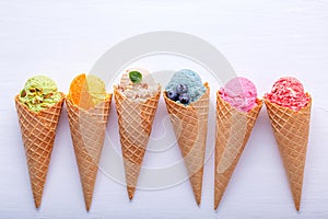 Various of ice cream flavor in cones blueberry ,strawberry ,pistachio ,almond ,orange and cherry setup on white wooden background