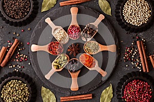 Various spices in wooden spoons on dark stone table.