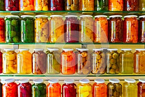 Various jars with Home Canning Fruits and Vegetables jam on glass shelves photo