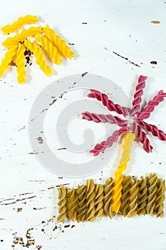 Various kinds of colored raw pasta on a white background, top view, in the form of flower fields and sun from food