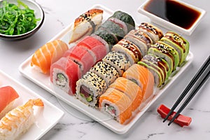 Various kinds of sushi placed on white square plate, seaweed salad and soy sauce in a bowl on the side