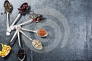 Various kinds of tea in spoons on dark slate background. Dry Tea assortment.